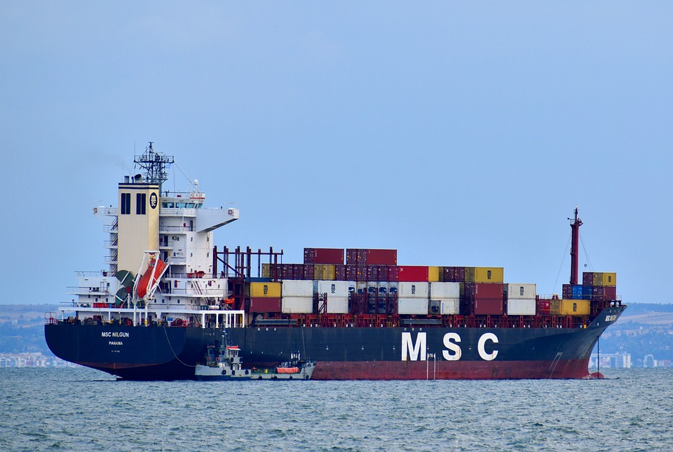 Los portacontenedores se pueden definir como buques mercantes, que con respecto a otros buques, posee un gran tamaño respecto a otros barcos comerciales, donde la eslora de suele rondar los 300 metros y con unas capacidades de hasta de 20.000 contenedores TEU.

Con respecto al manejo de estos buques, se pueden decir que estos son de difícil manejo en los puertos debido a su tamaño, lo que conlleva cierta peligrosidad tanto para el medioambiente como para las personas.

Sin embargo, estos barcos tienen una gran importancia para el funcionamiento de la vida cotidiana: ya que alrededor de 6.000 buques circulan en este momento con más de 20 millones de contenedores; esto quiere decir que el 90% de lo que consumimos a diario. Además, la capacidad de estos barcos hace que el transporte, por ejemplo, de unos pantalones ascienda a 12 céntimos y el de un teléfono móvil algo menos de 9 céntimos, un hecho que ha revolucionado el comercio internacional desde la introducción de los contenedores TEU.



Hay diferentes permisos que deben solicitar para que este tipo de buques se mueva, ya con el permiso de la autoridad, podemos distinguir tres acciones fundamentales para el atraque de portacontenedores: el practicaje, el remolcado y el amarre. Ahora veremos en qué consisten cada una de ellas. Definamos cada una de ellas:

Practicaje
El practicaje es la ayuda complementaria hasta el amarre al capitán del portacontenedores, que, aunque es un experto en navegación, puede no conocer las circunstancias locales de cada puerto. Así, un experto marino en rango de capitán mercante (práctico) estará a bordo del portacontenedores para asesorar en los movimientos del barco al capitán, aunque el práctico solo realiza su labor en calidad de asesoramiento, recayendo sobre el capitán toda la responsabilidad.

Las labores de practicaje son normalmente obligatorias para estos barcos, pues según la legislación todo barco superior a 500 GT (toneladas de registro bruto) o con mercancía peligrosa debe ser asistido. Además, en algunos puertos existe una figura denominada atalayador, cuya misión es vigilar el estado de la mar para notificar cambios de mareas, vientos, etc. y también ordenar el inicio del atraque cuando considere que las circunstancias son idóneas.



Remolcado
Los remolcadores guían al barco portacontenedores y lo empujan para facilitar las maniobras, siendo un servicio de obligado uso para estos buques mercantes. El número de remolcadores varía según el tamaño del barco, oscilando entre 1 y 4 y con una potencia que puede llegar hasta los 25.000 caballos de vapor. La dirección de estos buques depende del práctico, una figura que está presente en el puente de mando y en ocasiones también en uno de los remolcadores.

Amarre
Amarrar un barco es disponer las líneas de amarre de la embarcación de forma que estos queden fijados al muelle con seguridad, una tarea destinada en exclusiva para los amarradores. En el caso de los portacontenedores, habitualmente se trabaja contra bolardos y, cuando se trata de mercancías peligrosas, suelen valerse de sistemas de escape rápido, que optimizan los tiempos operativos, y facilitan desamarres rápidos e incluso remotos. Para el momento del contacto se requieren de los correspondientes sistemas de defensas, capacitados para absorber la energía generada y así evitan daños, tanto en los portacontenedores como en el propio muelle.

Cuando el barco se encuentra amarrado es cuando se da por finalizado el atraque y cuando comienza la carga y descarga del portacontenedores con grúas de distinto tamaño y características dependiendo del buque.

Recordemos que un buque es una embarcación marítima que posee una amplia cubierta resistente al clima y al mar, que cuenta a su vez con una buena estabilidad y puede navegar a grandes velocidades, permitiendo así que se pueda efectuar una navegación durante un periodo temporal considerable.

